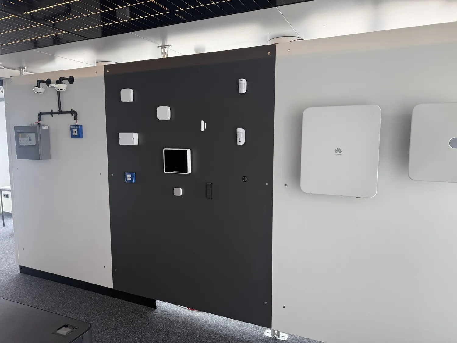 Technikwand im Showroom: Brandmeldezentrale, Ajax-Alarmtechnik, Huawei-Wechselrichter und Photovoltaik-Decke nebeneinander